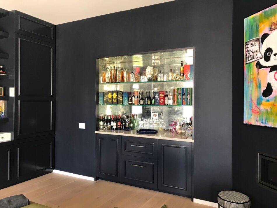 Modern home bar built into black cabinetry with glass shelves.