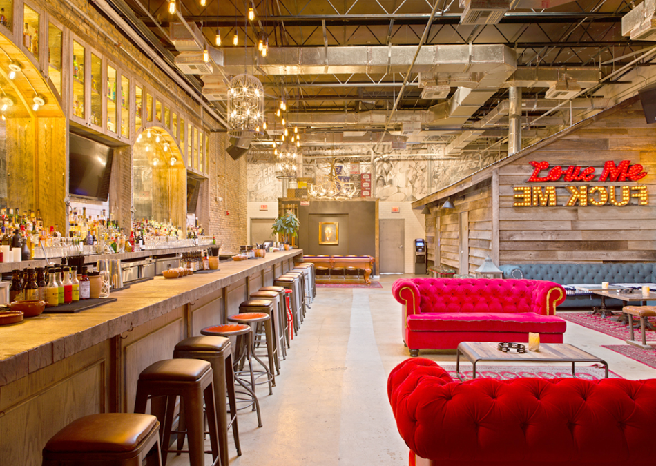 Industrial-style bar with red velvet sofas and exposed ceiling.